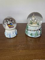 Front view of two snow globes: left Disney Mickey and Minnie Mouse 2006 snow globe, right Kurt S. Adler Christmas village church snow globe