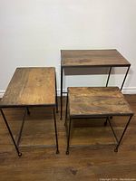 Three wood top and black steel frame nesting tables in view from an angle, showing sizes and wood grain top surfaces.