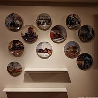Overview of all 11 round train plates mounted on a wall arranged in a roughly circular pattern, showing detailed paintings of trains in different settings.
