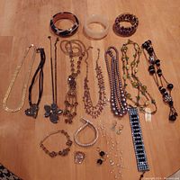 All costume jewelry items laid out on a wooden surface showing necklaces, bracelets, bangles, rings, and earrings arranged neatly in rows.