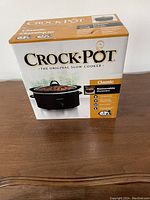 Photo of new Crock-Pot Classic 3 quart slow cooker in unopened original box on wooden surface.