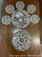 Top-down view of seven Czech crystal serving bowls: two large serving bowls (one footed) and five smaller individual bowls, all featuring pinwheel star cut designs laid out on a wood surface.