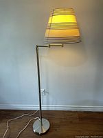 Front view of the silver floor lamp with blue striped fabric lampshade, showing the lamp lit in warm light.