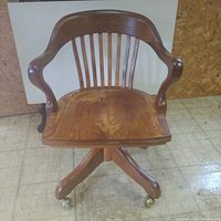 Front view of the vintage oak chair showing curved backrest with vertical slats and armrests, solid oak seat with visible wood grain and some discoloration.