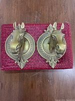 Top view of two brass horse head wall sconces resting on red woven mat.