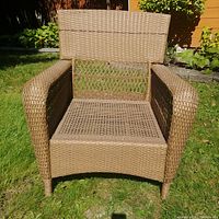 Front view of the wicker lawn chair showing the wide armrests, high back, and woven seat upholstery
