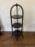 Front view of vintage dark wood three-tier pie stand showing three circular shelves and curved legs