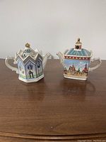 Two Sadler Russian Collection teapots displayed side by side on wood surface, showing detailed painted designs and unique shapes.