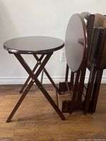 Side view of one wooden oval TV tray with crossed foldable legs and four trays stacked in the stand.