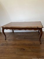 Full view of the vintage wood coffee table showing scalloped edges on the top and apron, four curved cabriole legs, and flat floor placement.