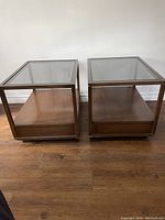 Pair of rectangular vintage wood end tables with removable glass tops shown side by side on a wood floor against a white wall.
