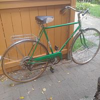 Side view of the vintage Sears bicycle showing green frame, rear rack, chrome fender, leather saddle, and pedals.