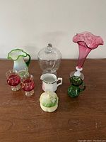 Photo showing eight assorted vintage vessels including two pitchers, a ruffled vase, two red glass cups, a clear glass jar, a ceramic creamer, and a ceramic jar.