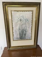 Front view of large framed white flower artwork showing detailed gold tone frame and scalloped edge on paper artwork.