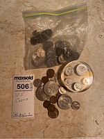 Photo of clear plastic bag with numerous US wheat pennies and some loose coins including silver and copper pieces on the table along with MaxSold lot card