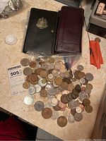 Overview photo showing two wallets and a large collection of assorted international coins and tokens spread on a surface.