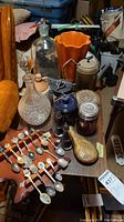 Photo of assortment showing collector spoons, decanter, shakers, flask, and orange ceramic vase.