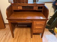 Front view showing oak rolltop desk facade, lower drawers and flat writing surface.