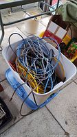Tote filled with various extension cords and power strips, cords tangled together inside a white plastic storage container with a blue lid underneath.