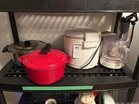 Side view of deep fryer, food processor, red Dutch oven, and metal pot on black shelf