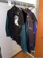 Four men's jackets hanging on hangers in a closet, visible colors black with green sleeves, brown, blue, and black with blue accents