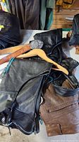 Photo showing black leather chaps with lacing, brown leather pants, leather belt, and wooden hanger