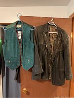 Photo showing teal Newport vest and black leather jacket hanging on door hooks, both on hangers.