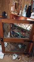 Front view of the wooden cabinet door with diamond pattern leaded glass panels, showing some interior shelves inside.