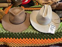 Two men's fur felt hats placed side by side on a crocheted blanket, showing overall shapes and colors.