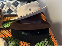 Three men's western hats stacked, showing cream wool hat on top and dark brown felt hat below on crocheted blanket
