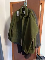 Photo of green Columbia Sportswear Company men's jacket size L hanging on hanger with others behind it on a door.