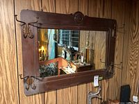 Front view of vintage wood framed mirror with hooks mounted on wall, showing the mirror surface and frame details.
