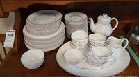 Photo showing stacked dinner plates, dessert plates, and teacups with the teapot in the background.