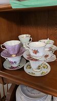 Photo showing stacked teacups and saucers of various designs and colors including purple, white with floral, and pastel colors
