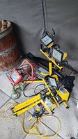 Photo showing multiple yellow work lights with stands, cords, and one smaller clamp-mounted orange light.
