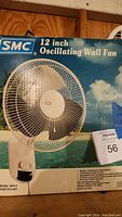 Photo of the new in box 12-inch oscillating wall fan with SMC branding on the packaging.
