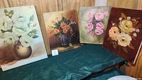 Four floral oil paintings by Consuelo Ingle shown on green cloth background. Various flower arrangements in different vases and backgrounds.