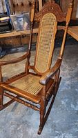 Full view of the antique rocking chair showing the cane back and seat, carved wood frame, and rocker base.
