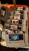 Stack of original Super Nintendo cartridges including Super Mario World, Tecmo Super Bowl, Bulls vs. Blazers, The Amazing Spider-Man, and others