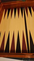 Close-up photo of wooden backgammon board showing classic triangle design with black, maroon, and cream points.