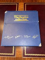 Blue textured box labeled 'The Beatles Collection' with gold lettering and Beatles signatures on top, showing corner wear and damage.