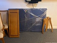 Disassembled wooden dining table components wrapped in moving blankets and plastic wrap, showing legs and table top panels.
