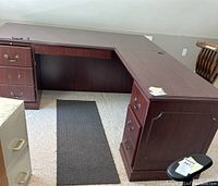 Photo of L-shaped executive desk showing drawers with silver-tone handles on both ends and leg space in the center, placed on carpet.