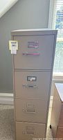 Front view of the beige metal file cabinet showing the four drawers with metal handles and label holders.