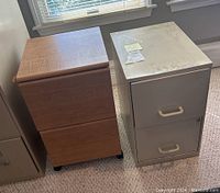 Photo showing side-by-side metal and wooden file cabinets on carpet near window with light gray and wood finish, visible wear on metal top surface, wooden cabinet on wheels.