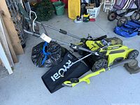 Ryobi push mower with grass catcher bag and string trimmer handle on top, black plastic bag behind