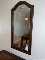 Front view of the wood framed wall mirror hanging on beige wall by a table with a dark wood finish.