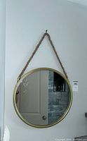 Front view of round mirror with gold frame and rope hanging on wall.
