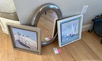 Two nautical prints and one oval metallic framed mirror are propped against a wall, showing size and framing details.