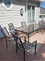 Six metal outdoor patio chairs including two rocking chairs around a rectangular metal and glass patio table on a wooden deck.